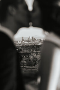 A slightly blurred image of a couple kissing with a city skyline in focus behind them.