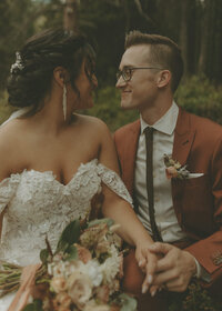 bride and groom sitting looking at each other beside each other in a forest and smiling at each other