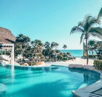Group of women gathered on a Tulum beach during a Kore Retreat, standing in a circle with raised arms in a powerful expression of unity, empowerment, and holistic healing by the ocean.