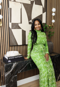 Josie Duncan wearing a blush duster, whote top, and jeans, posing i a kitchen and opening an upper cabinet door.
