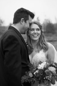 A newlywed couple standing close resting their heads together 