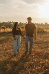Couple walking hand in hand through a golden farm field during sunset in Aiken SC captured by KateLens Photography.