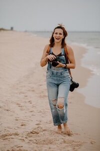 woman walking along shoreline holding cameras