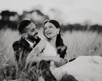Bride & groom sitting in a field laughing