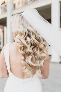 Groom gently embraces his bride outdoors as she closes her eyes in peace, highlighting her soft curls and diamond ring.