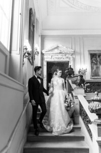 bride and groom walk down a grand staircase during their portraits at the Anderson House in Washington, D.C.
