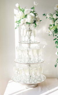 Champagne glasses tiered like a wedding cake with florals on top in a bright and airy setting