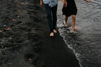 couple walking on black sand beach in two harbors minnesota during their engagement session take by lulle photo a minneosta wedding photographer