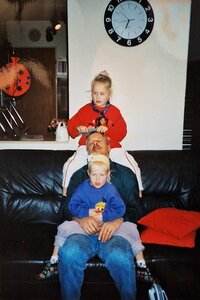 Foto uit jaren 90 vader heeft dochter op schoot en andere dochter zit op rand van de bank om haren te kammen van papa