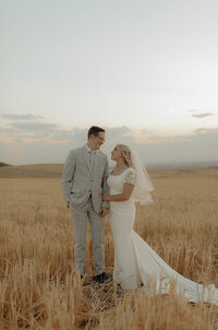 Bridal portraits taken in Idaho Falls, Idaho. A bride and groom stand side-by-side in a wheat holding hands.