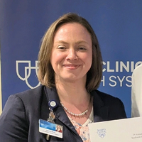 Carolyn smiling in front of a wall with the logo for "Mayo Clinic"