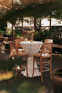 Outdoor evening reception setup at Blockhouse venue featuring elegant white cocktail tables and wooden chairs under string lights at dusk.