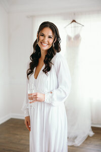 Bride holding a glass of champagne in her robe before she gets dressed on her wedding day.