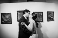 A newlywed couple kissing in front of a wall of art 