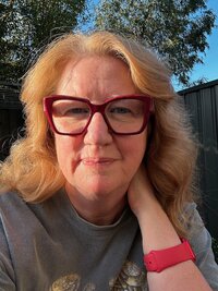 candid shot of Suzanne Harrison wearing a gray top and red glasses 