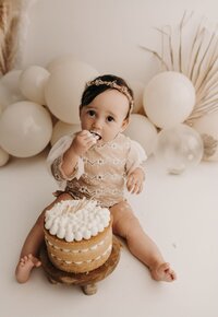 Joyful baby eating cake at their first birthday party in Mullingar, surrounded by balloons