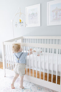 Young boy reaching to say hello to newborn sibling through crib