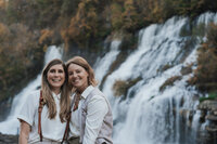 Two women embrace and smile near a Tennessee waterfall