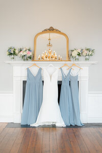 Bridal gown and blue bridesmaid dresses hanging from beautiful fireplace mantle