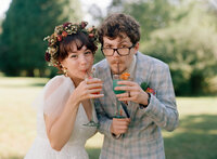 Film photo of a bride and groom sipping colorful cocktails through straws on a sunny lawn during their summer wedding in Massachusetts — captured by a film wedding photographer.