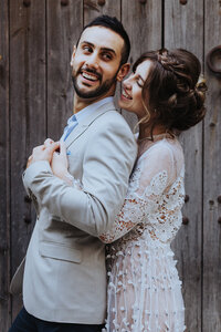 Elopement Photographer, woman hugs her husband from behind , they are both smiling before a wooden fence
