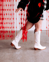 Close-up of white boots mid-step among red fringe streamers – styled detail shot from a concept-driven shoot by Mewphotovideo