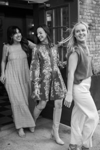 Black and white image of three women walking outside through a door