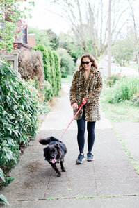 A woman in a leopard print coat walking her dog.