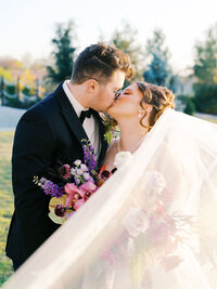 A bride and groom kiss, her veil flowing in front of them, at their Tulsa, Oklahoma wedding.