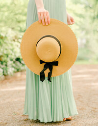 a woman holds a straw hat with a black bow.