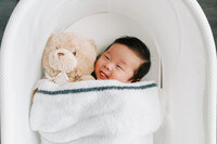Korean baby boy cuddling with his teddy bear in his snoo at his Alexandria VA home