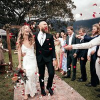 Relationship and intimacy coach with husband walking down the aisle at their wedding surrounded by wedding party and flower petals