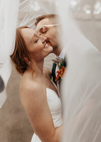 Groom kissing bride under veil