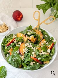 A spinach and nectarine salad topped with cashews and feta cheese.
