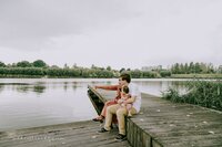 Father lifting baby girl into the air while mother looks on, standing on a lakeside dock.