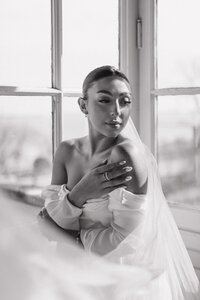 bride wearing her veil and wedding gown while standing in front of large window