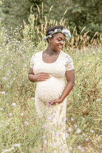 Woman in nature wearing a beige lace maternity dress with a floral crown for her maternity photo shoot.