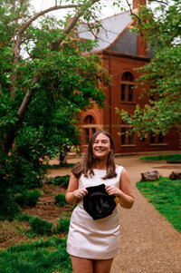 Senior holding cap outside copper building on Vanderbilt campus in the evening