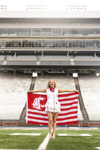 girl celebrating graduation with school flag in stadium wearing a little white dress