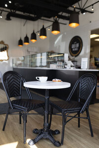 Two black café chairs at a white table with a coffee cup and pastry inside Gold Leaf Pastries bakery in Kamloops BC.