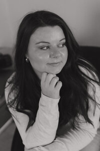 A black and white photo of Michaela resting her chin on her hand, looking off to the side and smiling softly.