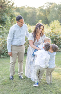 Candid photo of a family of five laughing and playing together in a grassy field during a golden-hour family photo session in Connecticut.