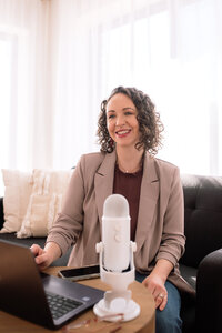 A woman sitting on a sofe in front of a podcast mic.