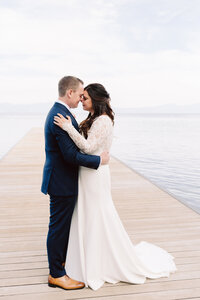 bride and groom standing next to lake with mountains in background