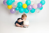 Edmonton studio cake smash on white savage seamless paper backdrop with purple, teal, yellow, pink, and confetti balloons