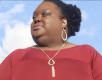 african american woman with natural hair in a blue button up leaning on a dining table