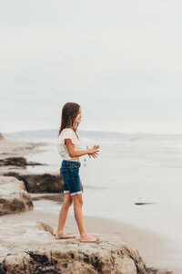 a young girl stands on a rock at Del Mar beach looking at the ocean in San Diego