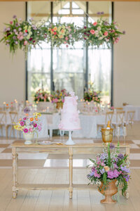 Wedding cake displayed beneath a hanging floral installation at an elegant Oklahoma estate wedding.