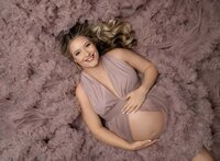 Pregnant Mom in pink dress laying down on bed of tulle ruffles. Photo taken at Atlanta Photography Studio in Woodstock, GA.