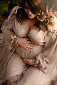 Pregnant mother in a silk gown holding her belly.  Portrait by Brittany Danielle.